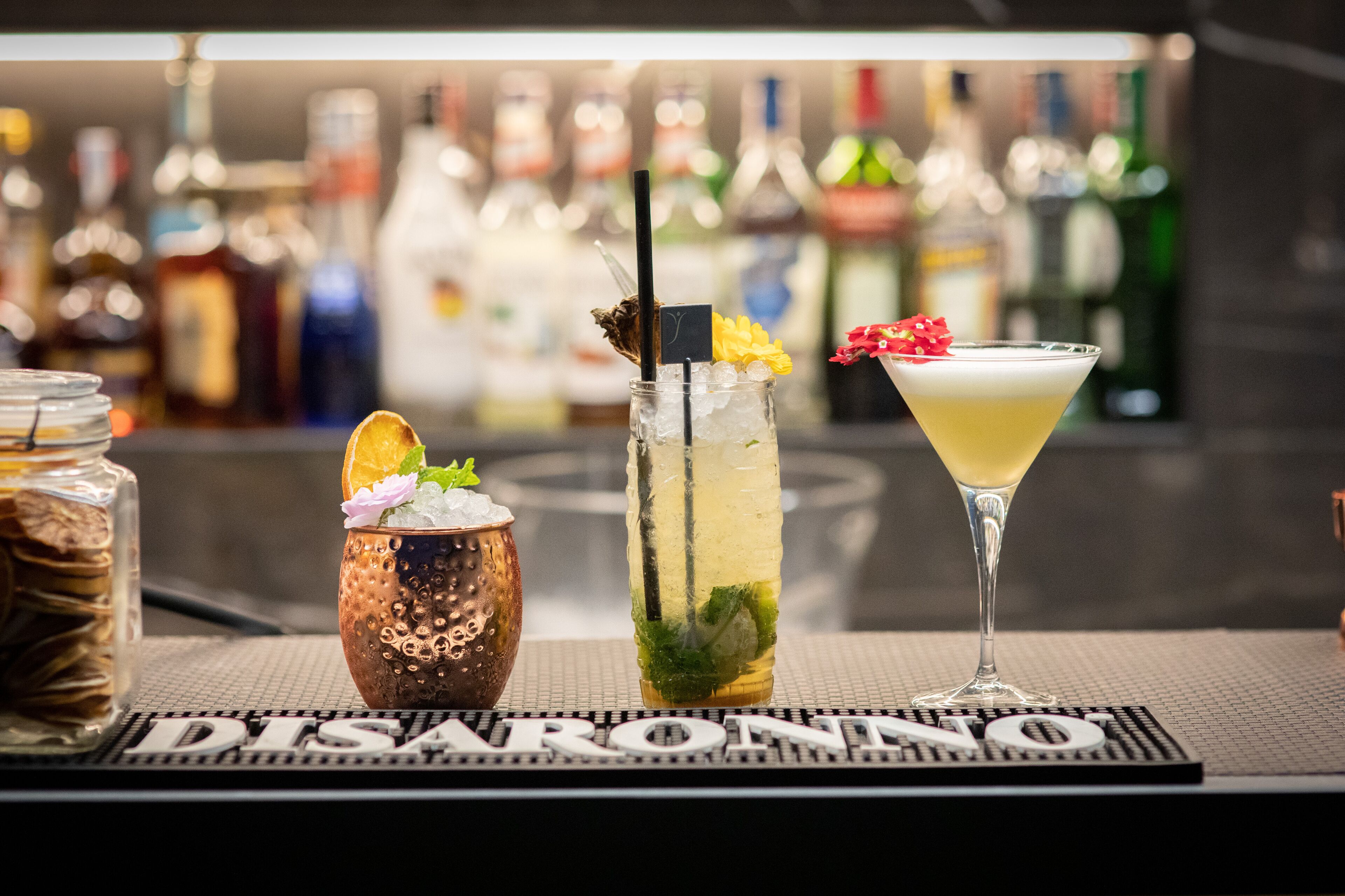 Three drinks on a bar counter with a blurred background of bottles.