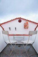 Un pequeño espacio al aire libre con una mesa y dos sillas, una jaula decorativa en la pared y un suelo de baldosas geométricas.