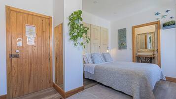 Un dormitorio con puerta de madera, una cama con colcha azul, una planta colgante y un espejo con marco decorativo.