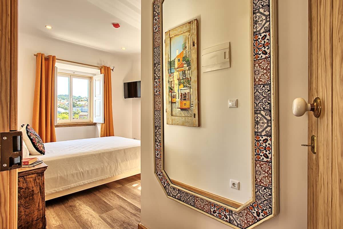 Ein Schlafzimmer mit einem Bett, einem Fenster mit Vorhängen, einem Bild an der Wand und einer Holztür.