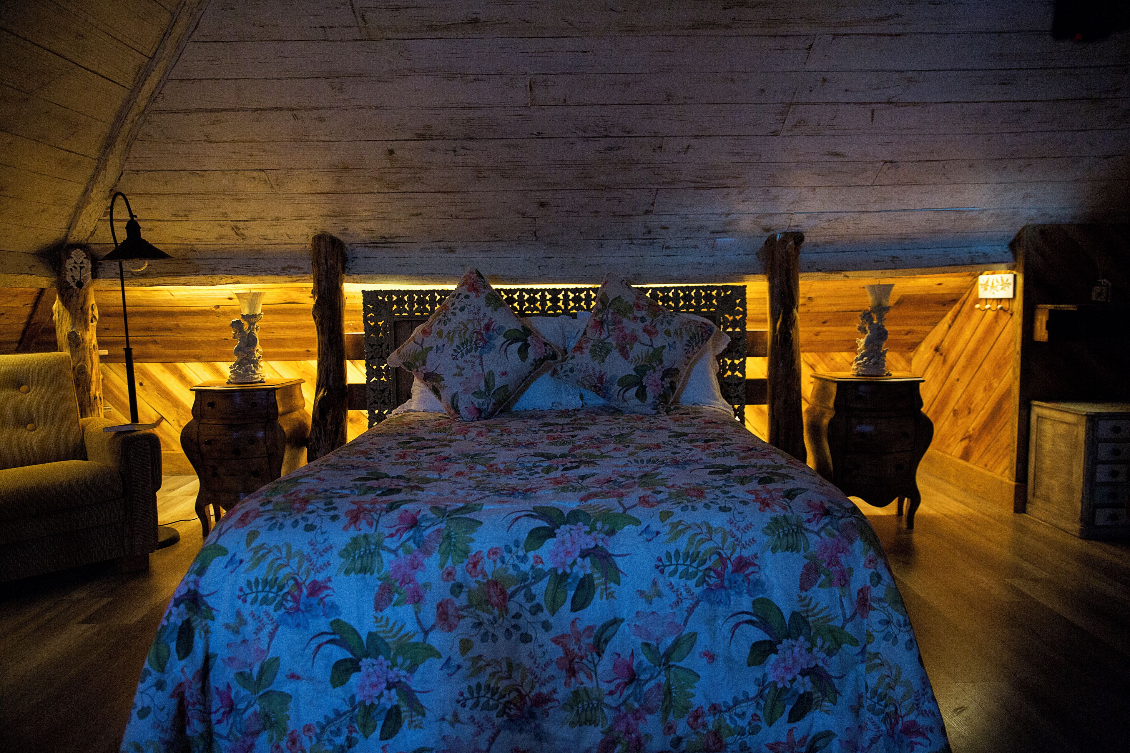 Um quarto de sótão acolhedor com colcha de flores, paredes de madeira e teto inclinado.
