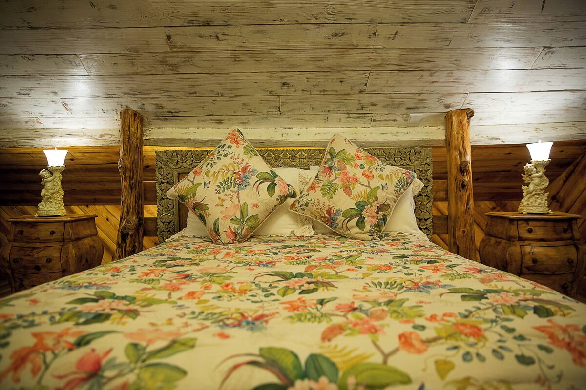 Ein Bett mit floraler Bettwäsche, einem Holzkopfstück und Nachttischen mit Lampen.