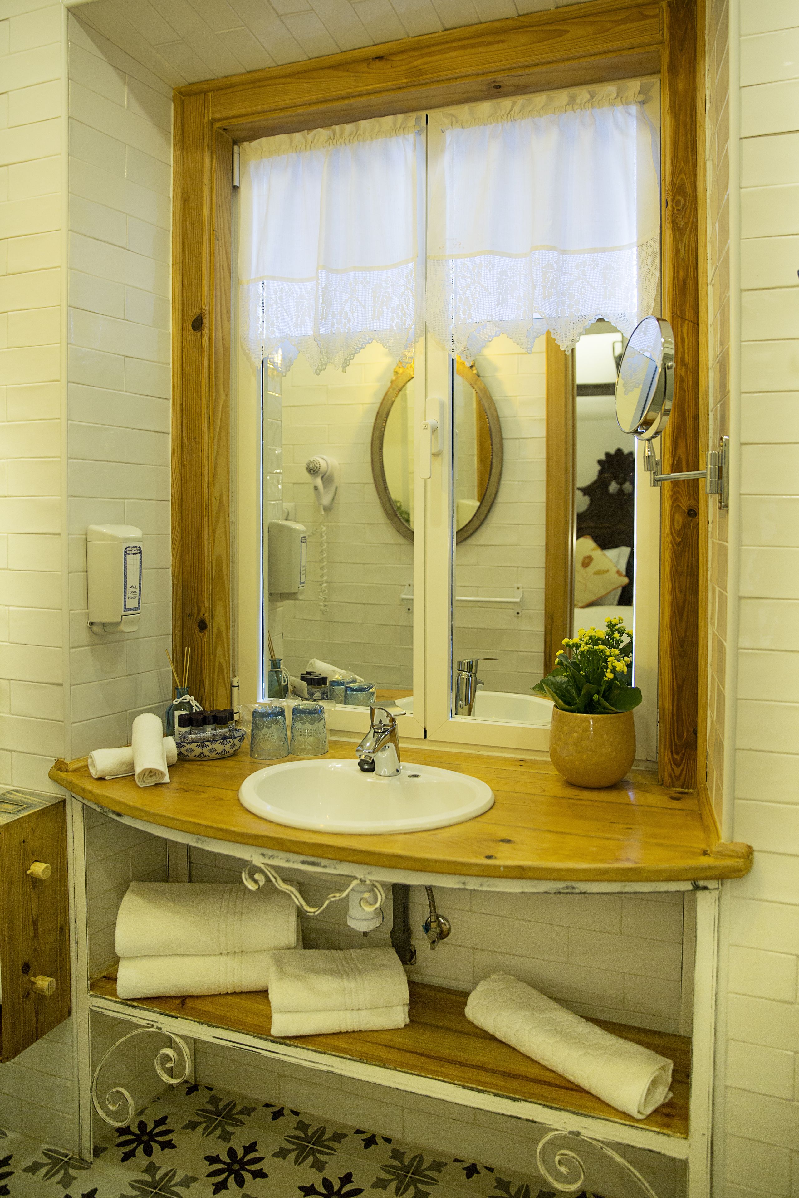 Une salle de bain avec un meuble-lavabo en bois, un lavabo blanc et un miroir. Il y a des serviettes sur l’étagère et une plante en pot sur le comptoir.