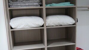 Een houten garderobe met meerdere planken en lades, waarvan sommige gevuld zijn met opgevouwen dekens en kussens.