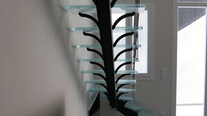 Een moderne trap met glazen balustrades en een zwarte centrale draagbalk.