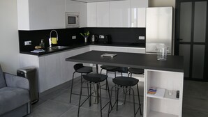 Een moderne keuken met witte kastjes, een zwart aanrecht, een ingebouwde magnetron en een koelkast. Er staan vier zwarte barkrukken bij het eiland.