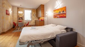 A compact hotel room with a bed, a small desk, a chair, and a kitchenette. - Beautiful stone flat for 4 in the Rue des Antiquaires (Bordeaux)