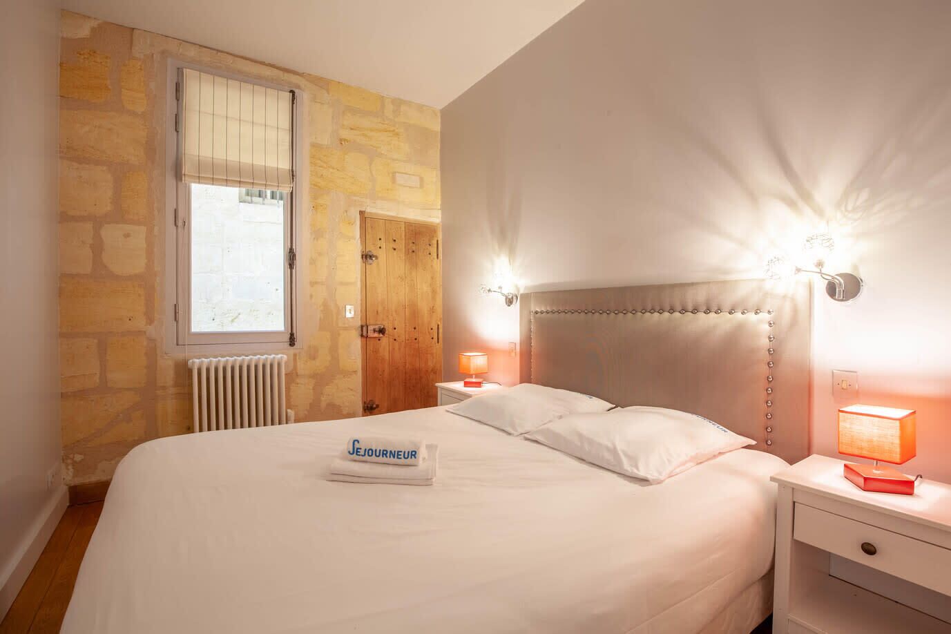 Ein Hotelzimmer mit Steinwand, Holztür, Bett mit weißer Bettwäsche und zwei Nachttischlampen.
