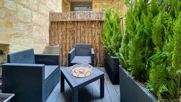 A courtyard with wicker furniture, a bamboo fence, and potted plants. - Beautiful stone flat for 4 in the Rue des Antiquaires (Bordeaux)