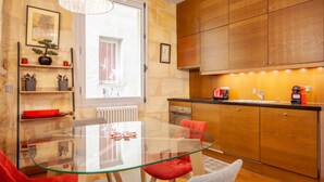 A modern kitchen with wooden cabinets, a glass dining table, and red chairs. - Beautiful stone flat for 4 in the Rue des Antiquaires (Bordeaux)