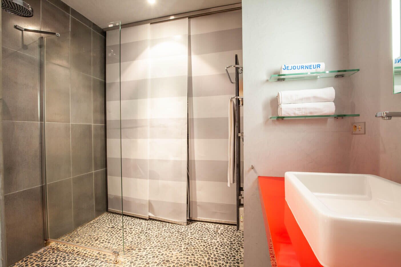 Een moderne badkamer met een douchecabine van glas, een wit bad en een glazen plankje met een handdoek.