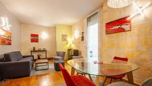 A modern living room with a glass dining table, grey sofas, and a red chair. - Beautiful stone flat for 4 in the Rue des Antiquaires (Bordeaux)