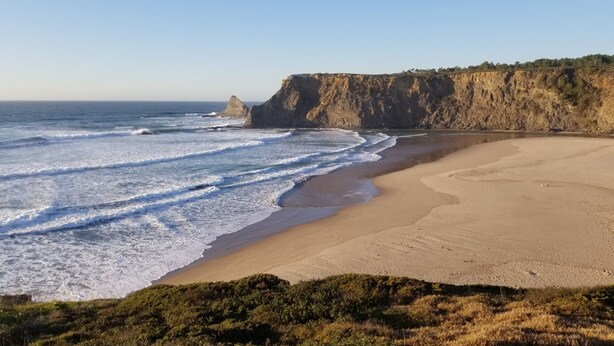 Una playa con un acantilado rocoso y olas rompiendo en la orilla.