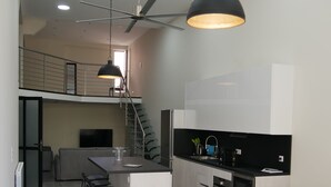 A modern kitchen with a central island, bar stools, a dining table with a patterned tablecloth, and a staircase leading to an upper level. - Large chic and modern loft, industrial decor (Beausoleil)