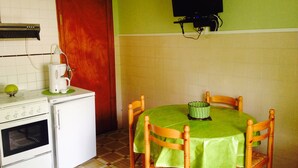Una pequeña cocina con estufa, cafetera y una mesa con sillas.