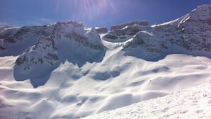 Paisaje montañoso cubierto de nieve, con picos escarpados y cielo despejado.