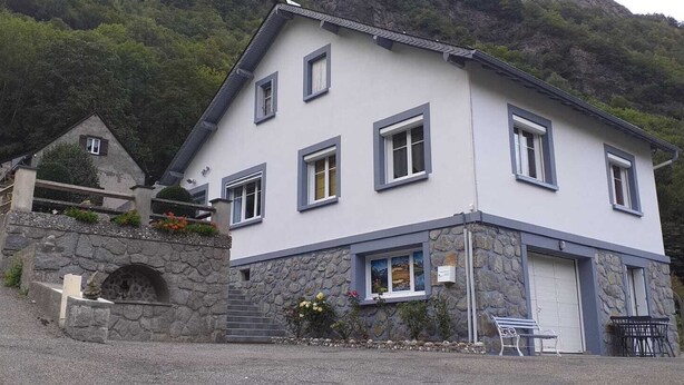 Un edificio de dos pisos con fachada de piedra, múltiples ventanas y un pequeño porche con escalones de acceso.