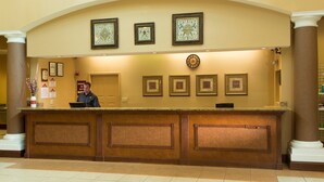 A reception desk with framed artwork above, a clock, and a man seated behind it. - Suite in Orlando | Access to Shared Pool/Hot Tub (Orlando)