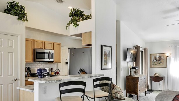 A modern kitchen with a central island, two bar stools, and wooden cabinets.