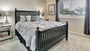 A bedroom with a bed, a nightstand, a lamp, a ceiling fan, and a window with blinds.