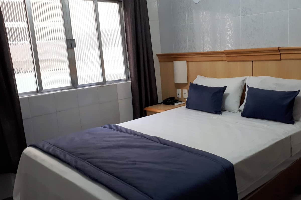 A hotel room with a bed, a bedside table with a lamp, a telephone, and a small bedside cabinet.