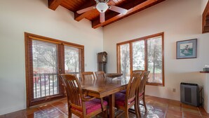 Un comedor con mesa y sillas de madera, ventilador de techo y ventanas grandes con persianas.