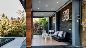 Un interior moderno con un sofá de cuero negro, una silla blanca y una mesita. Se ve una escalera que conduce a un espacio exterior con plantas y vistas al cielo.