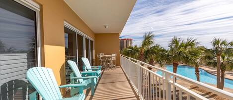 Un balcón con sillas Adirondack, piscina y palmeras.