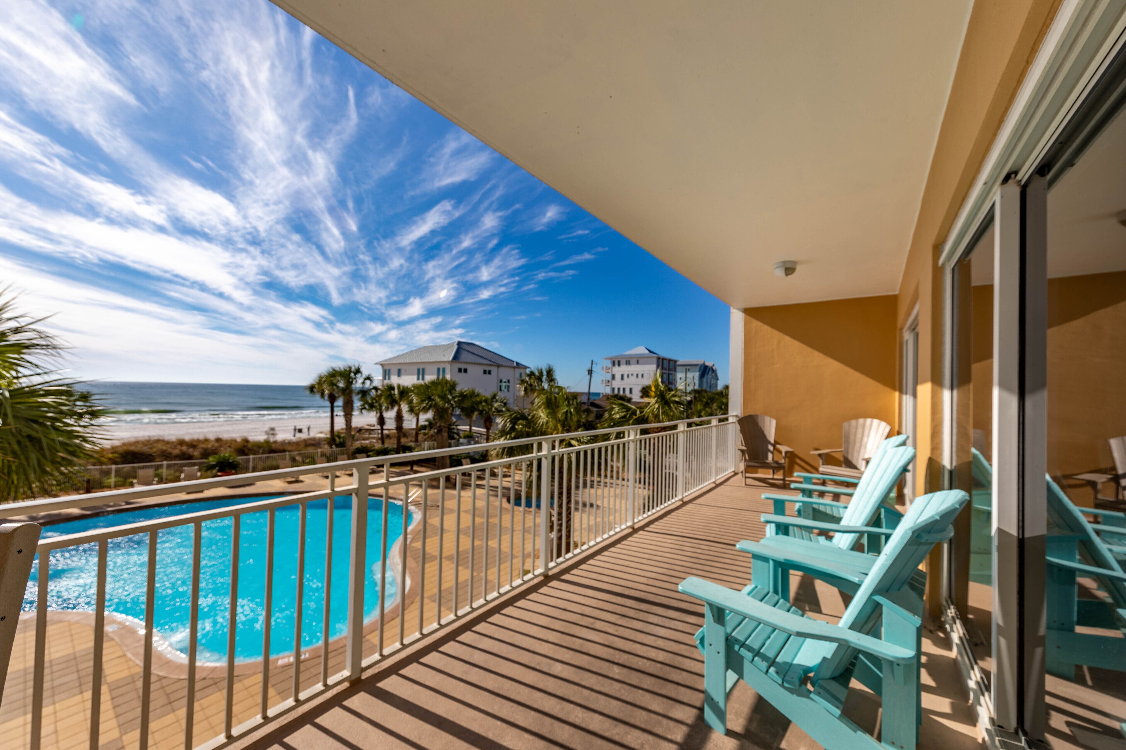 A balcony with a pool, beach view, and turquoise chairs.