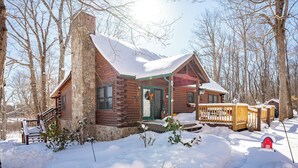 A log cabin with a stone chimney, wooden deck, and a red mailbox. - Woodsy Retreat w/ Fireplace, Hot Tub & Fire Pit (McHenry)