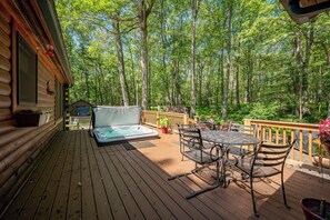 Una terraza de madera con un jacuzzi, mobiliario exterior y vistas a un bosque.