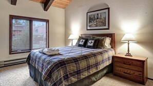 A bedroom with a bed, two bedside lamps, a nightstand, a framed picture on the wall, and a window with blinds. - Sunrise 35: Spacious, quiet (Mammoth Lakes)