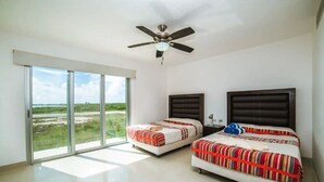 Un dormitorio con dos camas, un ventilador de techo y un amplio ventanal corredera con vistas al paisaje.