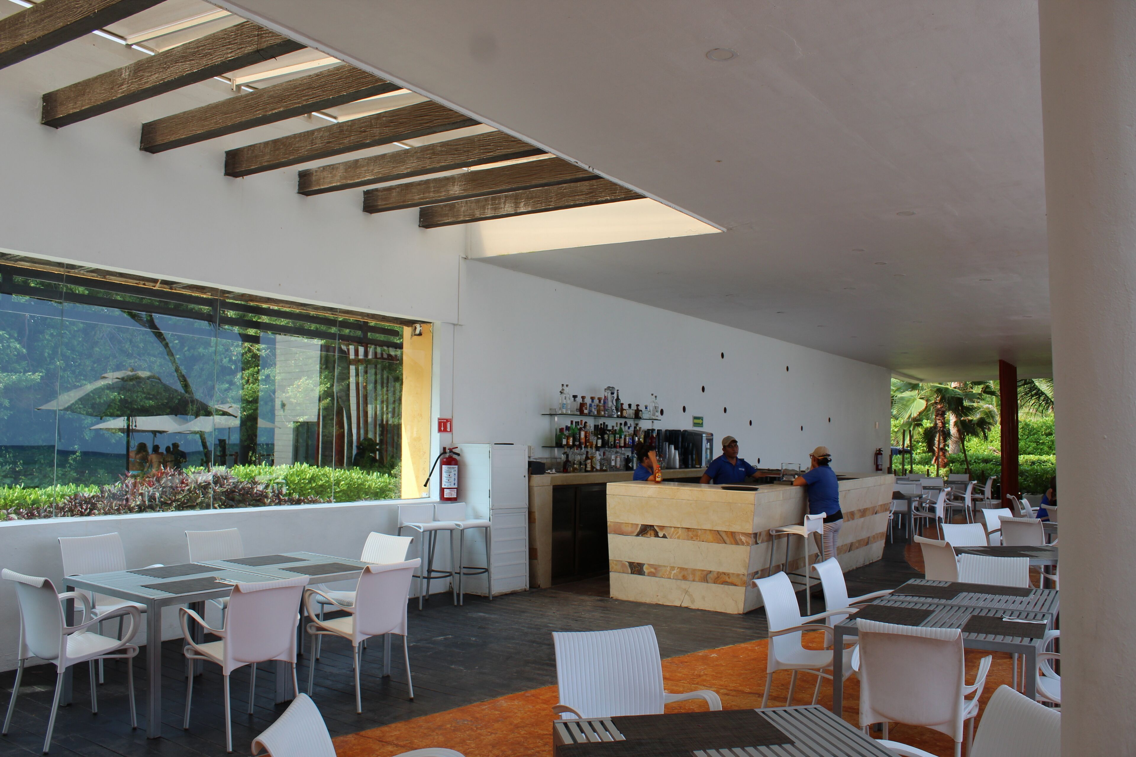 Un espace extérieur aménagé avec des tables et des chaises, un comptoir de bar et une vue sur la verdure grâce à de grandes fenêtres.