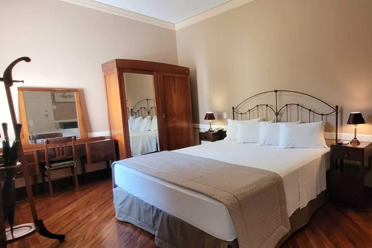 Habitación de hotel ordenada con cama, mesitas de noche, un espejo, armario y un mueble pequeño.