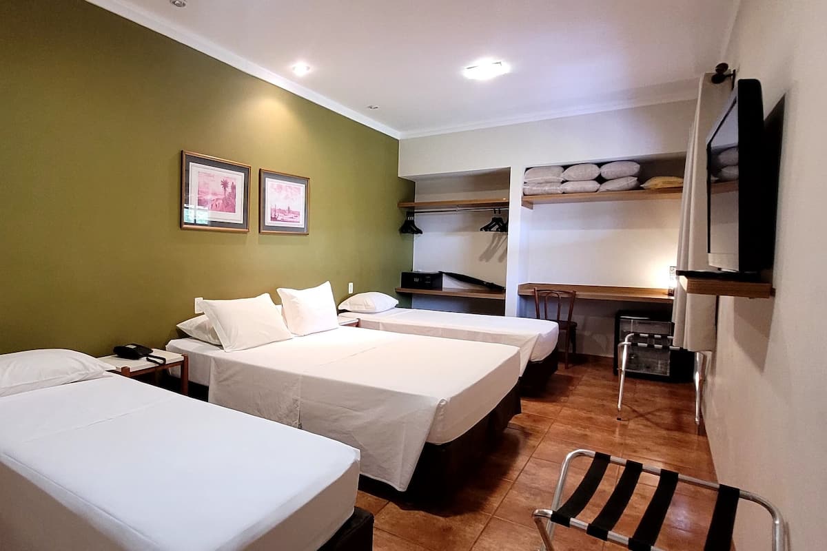Habitación de hotel con dos camas individuales, un escritorio pequeño con teléfono, un televisor montado en la pared y un armario con estantes.