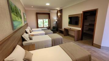 A hotel room with three single beds, a desk with a computer, a TV, and a large window.