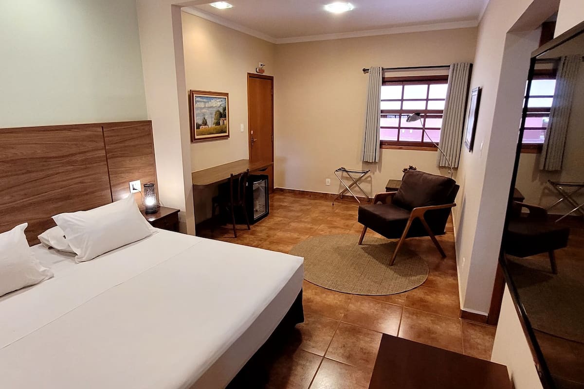 Habitación de hotel con cama, escritorio, silla, mesita y ventana con cortinas.