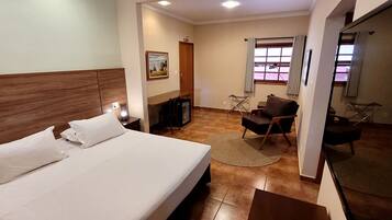 A hotel room with a bed, a desk, a chair, a small table, and a window with curtains.