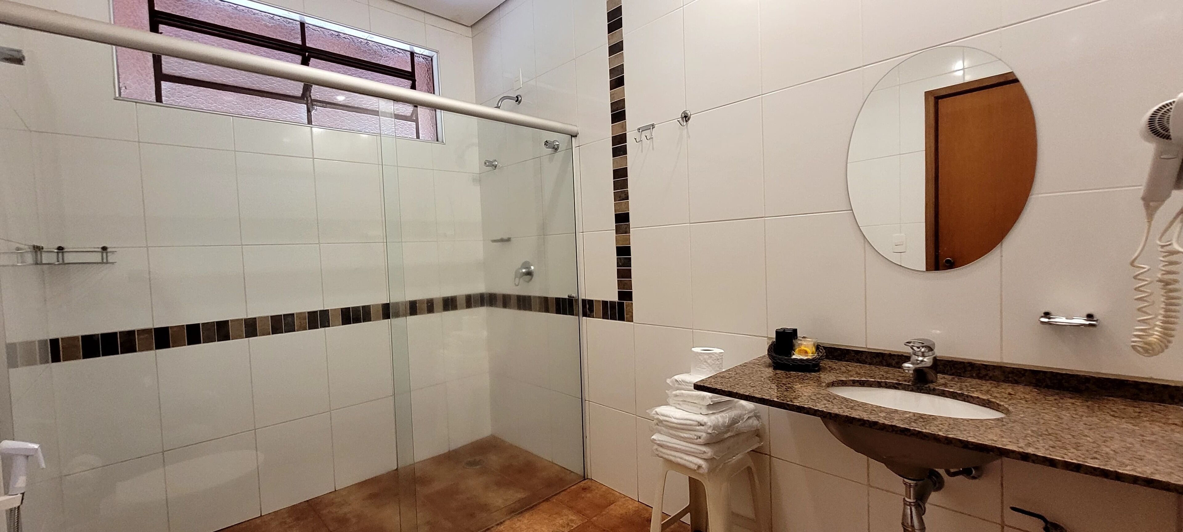A modern bathroom with a glass shower enclosure, a sink with a granite countertop, and a round mirror.