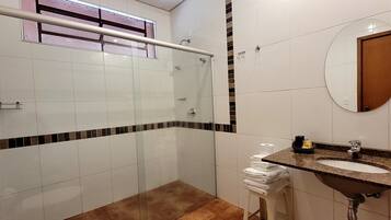 A modern bathroom with a glass shower enclosure, a sink with a granite countertop, and a round mirror.