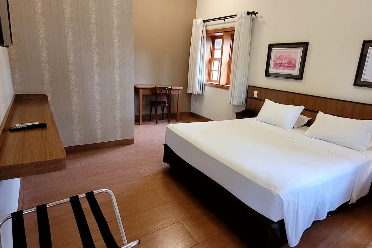 Habitación de hotel con cama, mesita de noche, lámpara, silla, escritorio y televisor instalado en la pared.