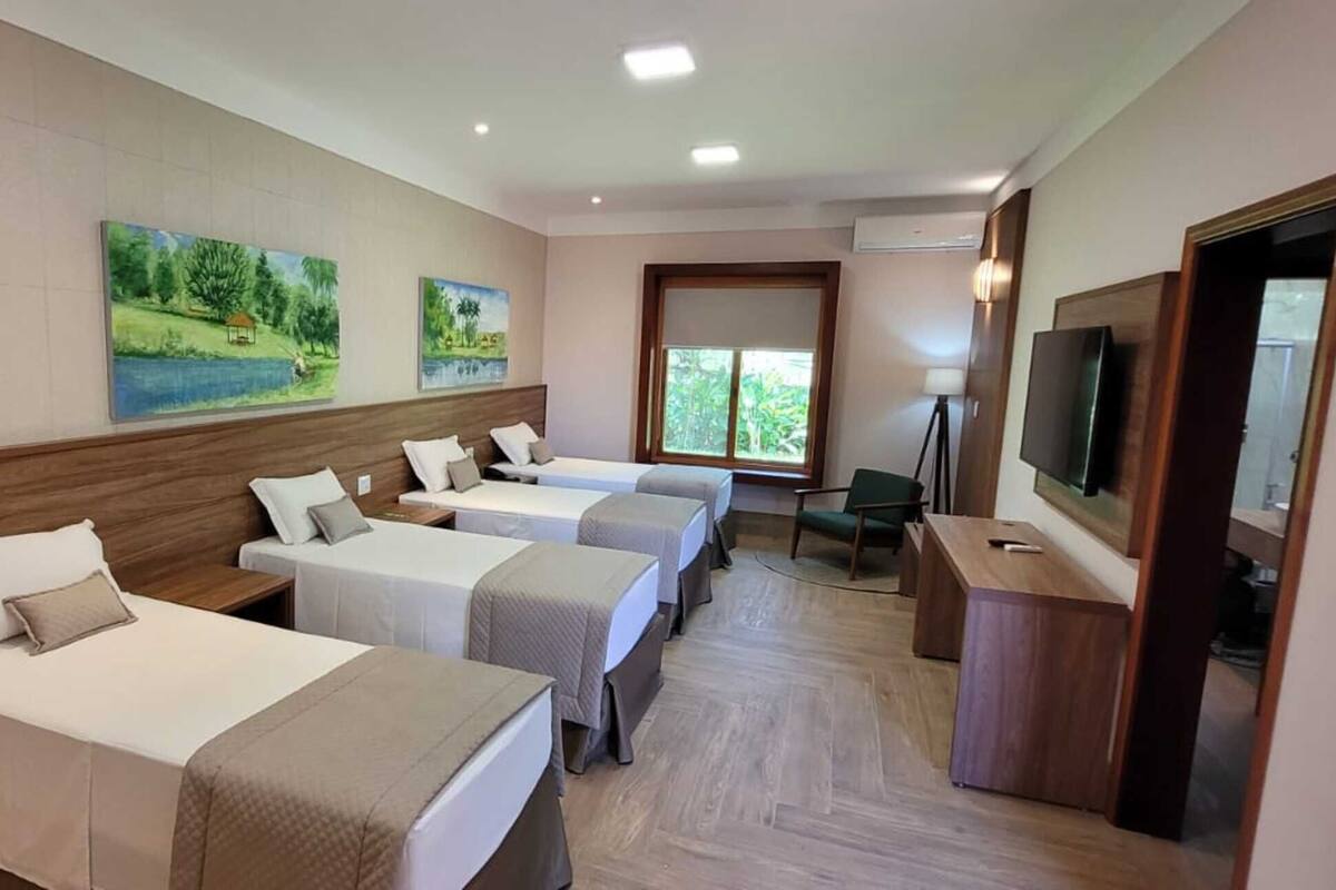 Una habitación de hotel con cuatro camas individuales, un televisor y obras de arte en las paredes.