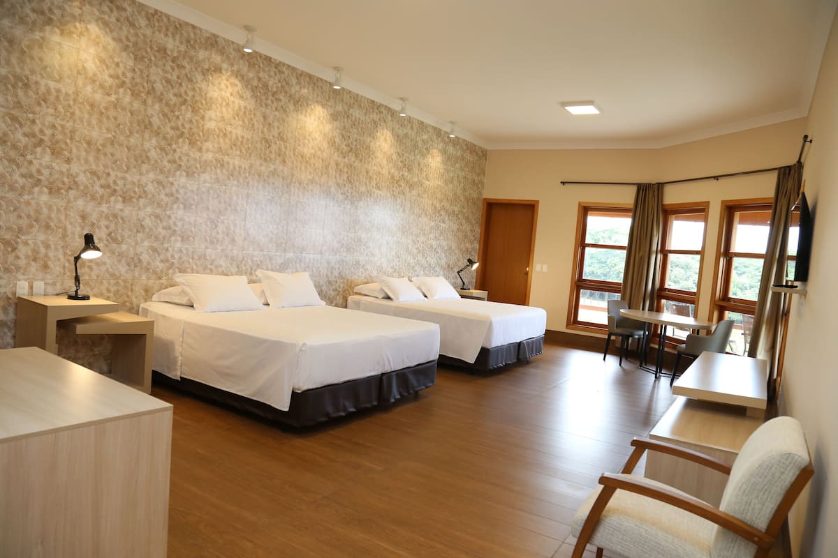 Habitación de hotel con dos camas, un escritorio y una zona de comedor con vistas a zonas verdes.