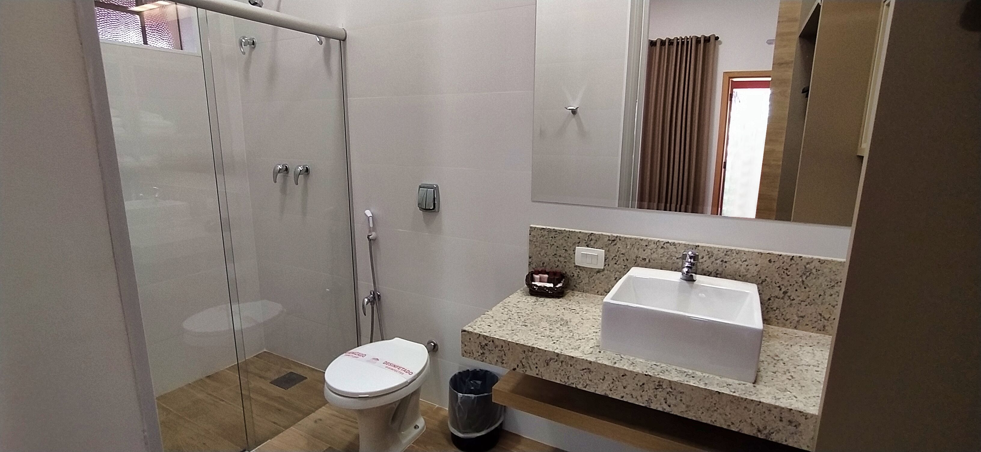 A bathroom with a glass shower enclosure, a white toilet, a sink with a granite countertop, and a mirror above the sink.