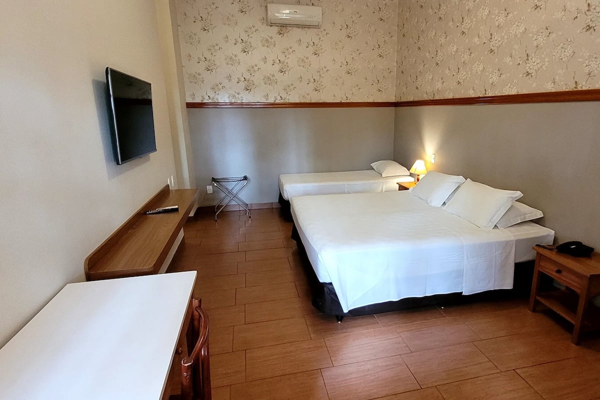 Habitación de hotel con dos camas, televisión, una mesita y suelo de madera.