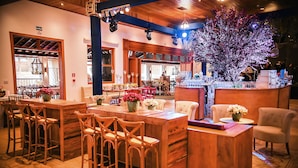 A bar area with wooden furniture, bar stools, and a large tree with lights.