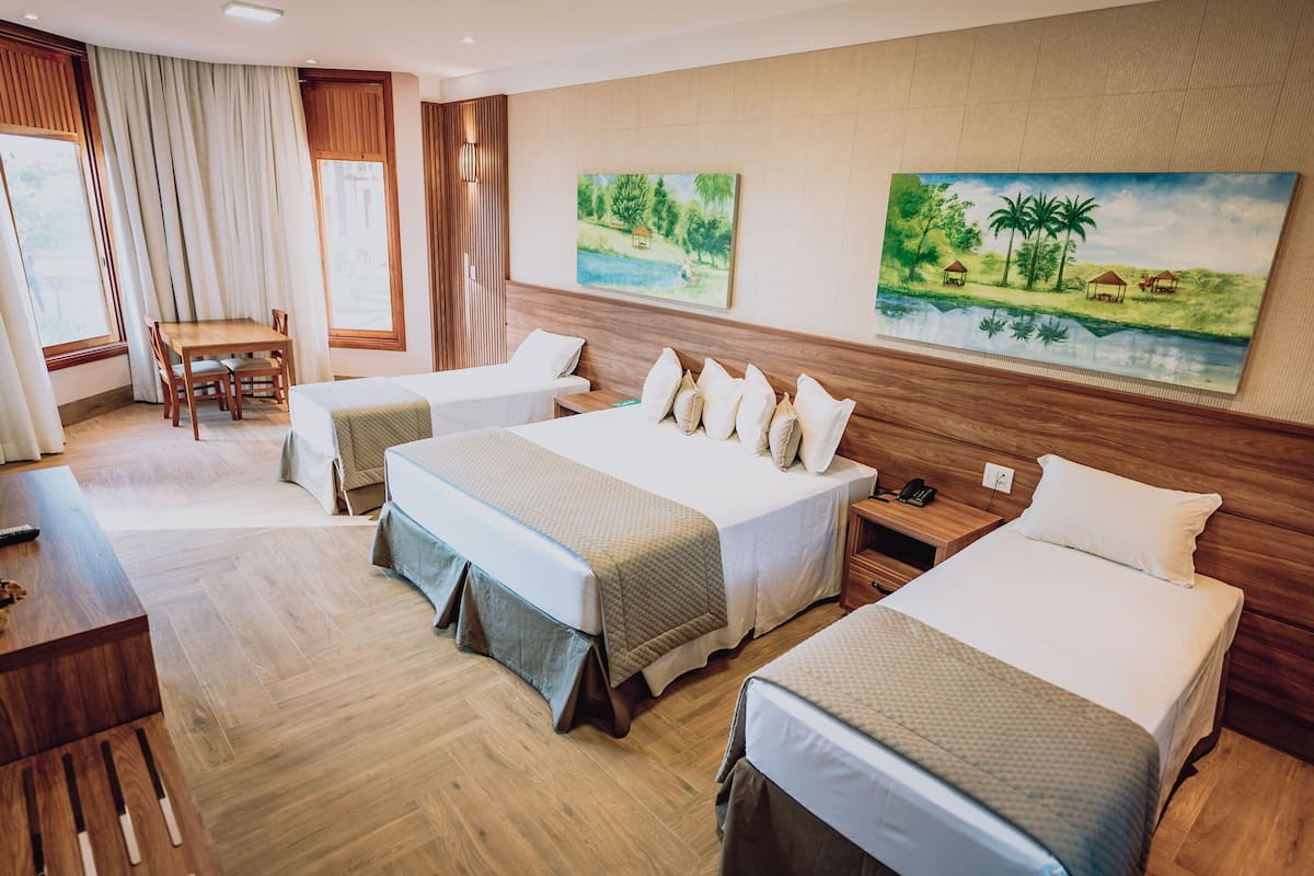 Habitación de hotel con tres camas, un escritorio de madera, una silla y dos cuadros en la pared.