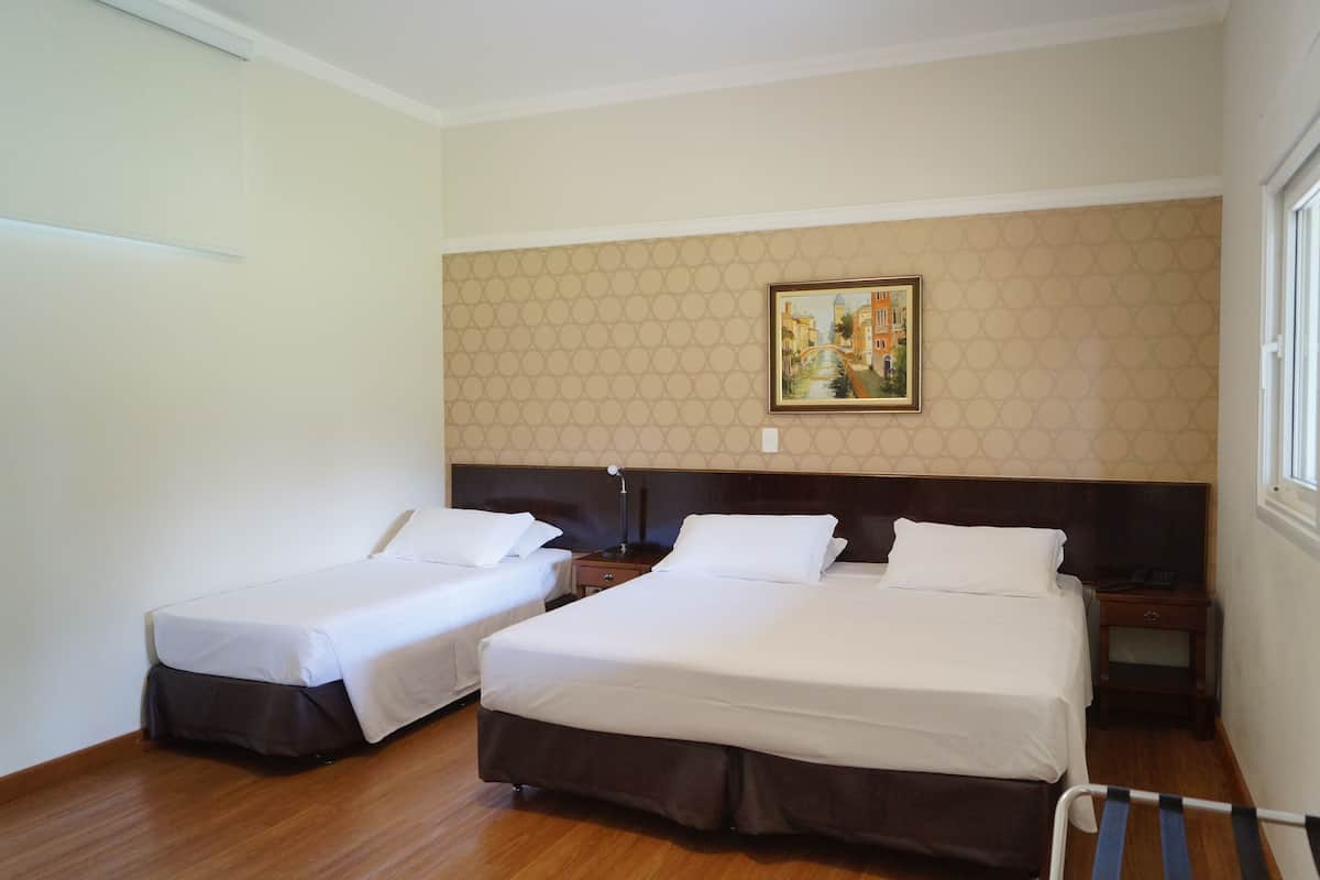 Una habitación de hotel con dos camas individuales, piso de madera, un cuadro en la pared y una ventana.