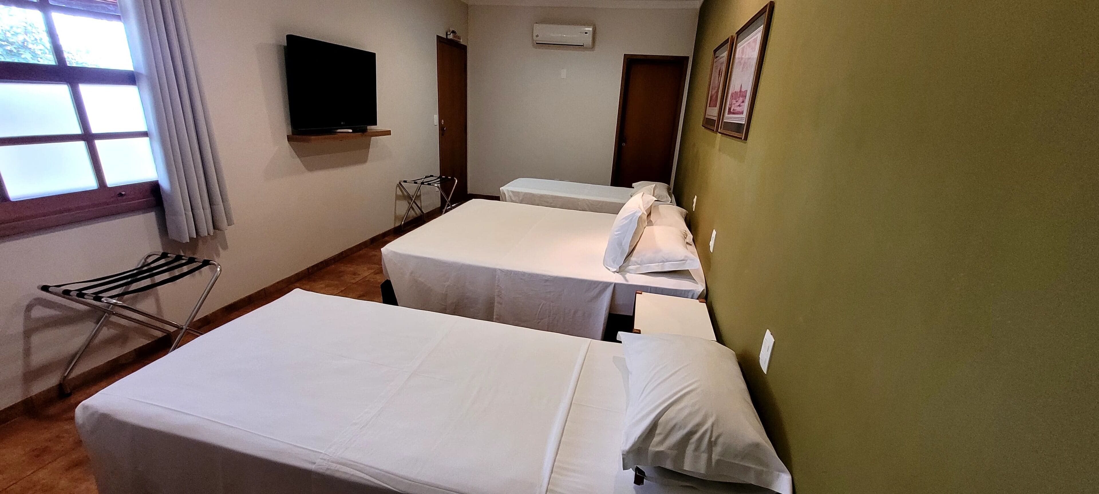 Una camera d'albergo con due letti, una TV a parete, una finestra con tende e un piccolo tavolo con una sedia.